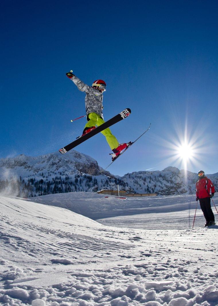 Skier jumping off snow ramp under clear blue sky in alpine ski resort